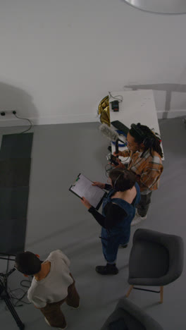 Vertical-Video-Overhead-Shot-Of-Female-Director-With-Production-Assistant-And-Sound-Recordist-Working-On-Film-Set-Shooting-Movie-Or-Video-In-Studio